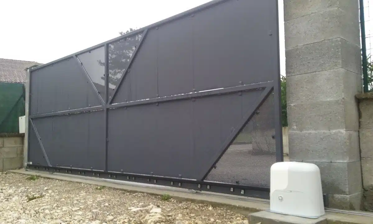Portail coulissant fermé et son moteur blanc posé au sol